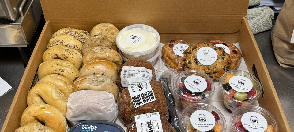 A box of bagel items including 2 dozen bagels with some fruit cups and fruit muffins.